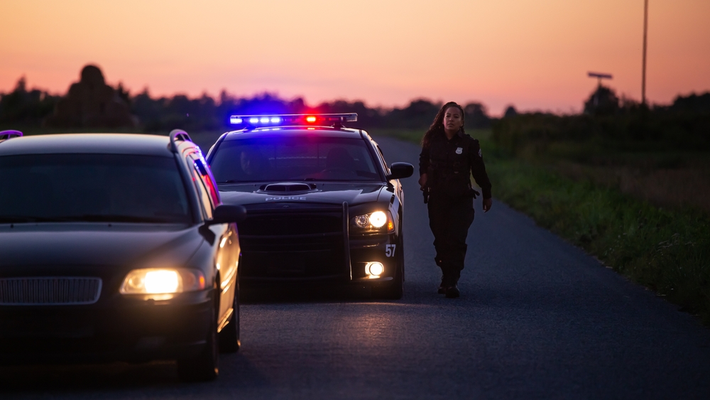 Police officer approaches a car, pulled over on the side of the road